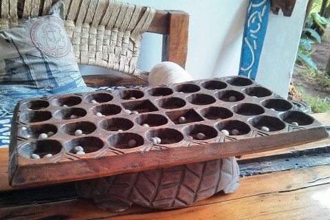 Ein Bao-Spielbrett aus Holz, das aus einer Holzplatte mit 32 Mulden besteht. In den Mulden befinden sich je zwei Pflanzensamen, die als Spielsteine verwendet werden.