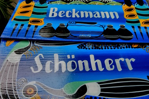 Das Foto zeigt zwei Schilder, die im Stil der tansanischen Tinga-Tinga-Kunst bemalt wurden