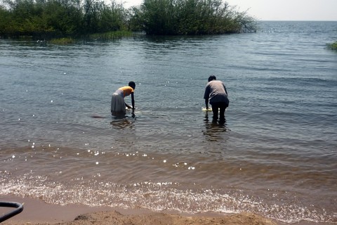Das Bild zeigt ein Mädchen und einen Mann, die Wasserkanister im Viktoriasee befüllen